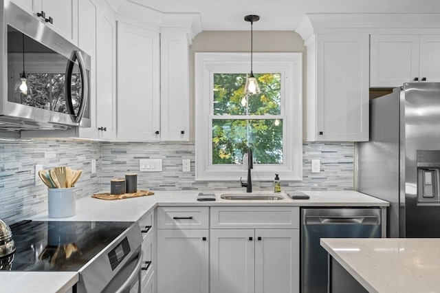 kitchen with tasteful backsplash, white cabinets, stainless steel appliances, pendant lighting, and a sink