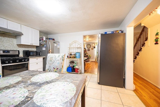 kitchen featuring appliances with stainless steel finishes, decorative backsplash, a textured ceiling, white cabinetry, and light tile patterned flooring