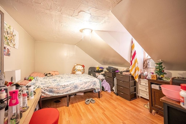 bedroom with a textured ceiling, vaulted ceiling, and light hardwood / wood-style flooring