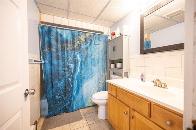 bathroom featuring toilet, a paneled ceiling, tile patterned floors, backsplash, and vanity