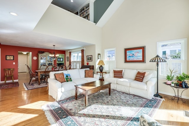 living room featuring light wood-type flooring, a notable chandelier, and a high ceiling