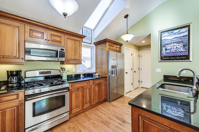 kitchen with lofted ceiling with skylight, light wood-type flooring, appliances with stainless steel finishes, and sink