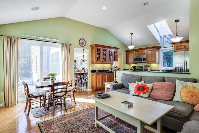 living room with vaulted ceiling with skylight, a chandelier, sink, and light hardwood / wood-style flooring