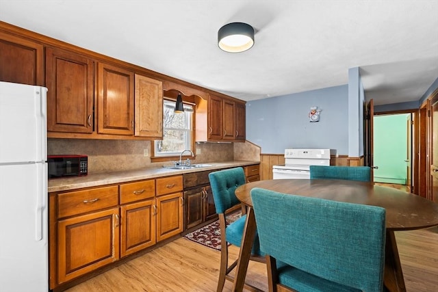 kitchen with sink, white appliances, baseboard heating, light hardwood / wood-style floors, and decorative backsplash