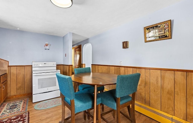 dining area with a baseboard heating unit, light hardwood / wood-style flooring, and wood walls