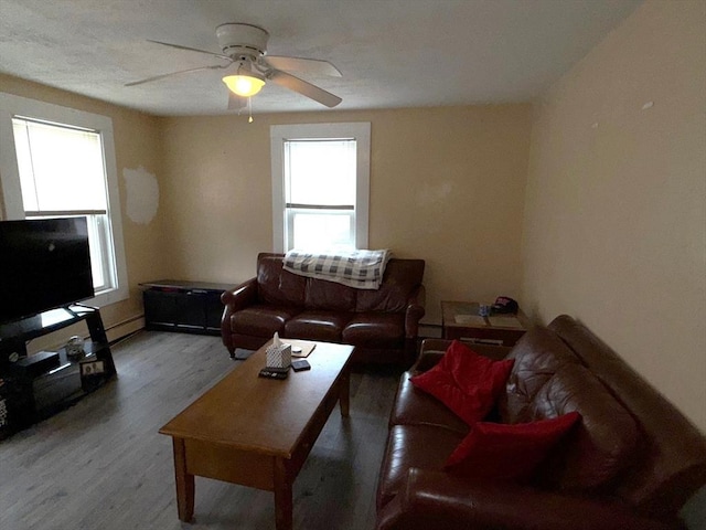 living room featuring baseboard heating, wood finished floors, and a ceiling fan