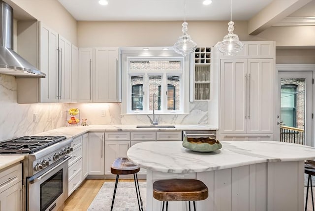 kitchen with stainless steel appliances, wall chimney range hood, a sink, a breakfast bar area, and decorative backsplash