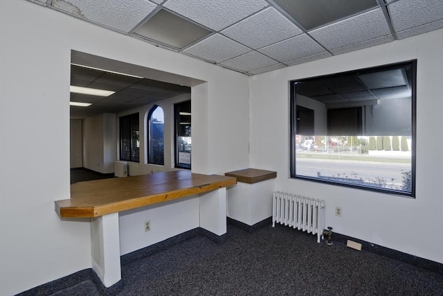 interior space with radiator, dark colored carpet, baseboards, and a paneled ceiling