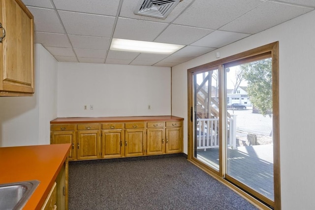 kitchen with a sink, brown cabinetry, visible vents, a drop ceiling, and dark carpet