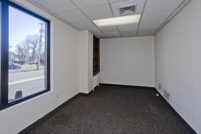 empty room with a paneled ceiling, dark carpet, and visible vents