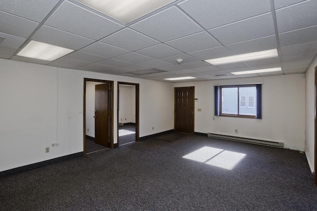 empty room with dark carpet, a drop ceiling, baseboards, and a baseboard heating unit