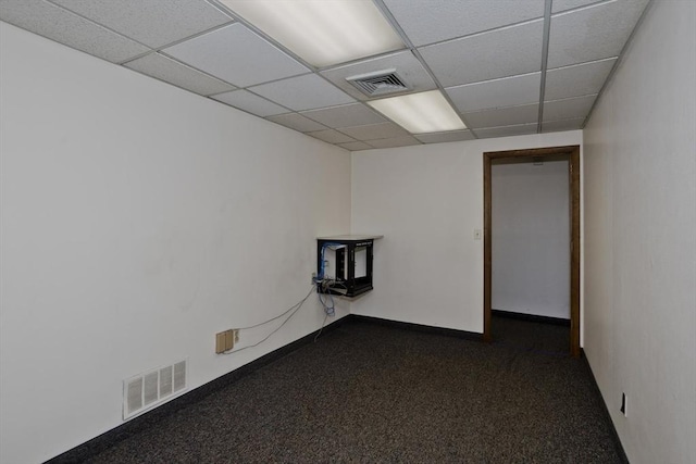 empty room with a wood stove, dark carpet, visible vents, and a drop ceiling