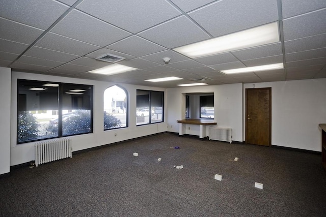 carpeted spare room with a drop ceiling, visible vents, and radiator heating unit