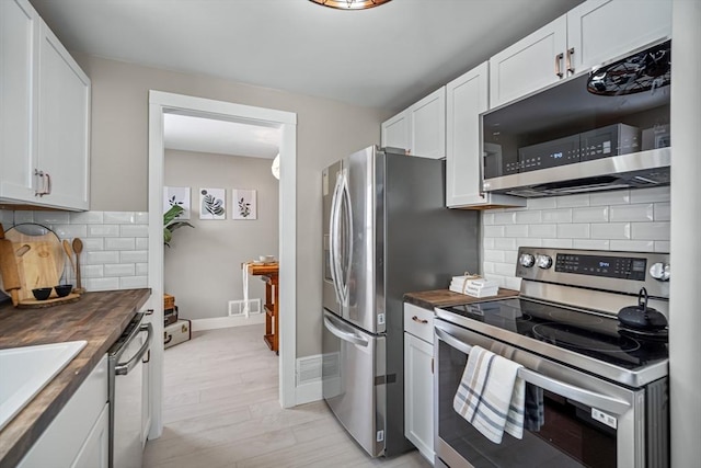 kitchen featuring wood counters, decorative backsplash, stainless steel appliances, and white cabinets