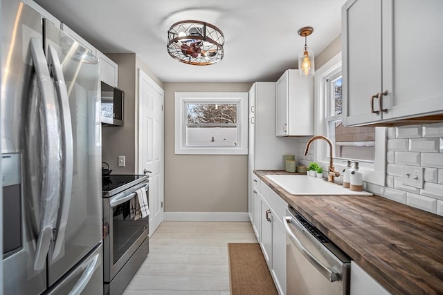 kitchen featuring butcher block countertops, white cabinetry, sink, hanging light fixtures, and stainless steel appliances