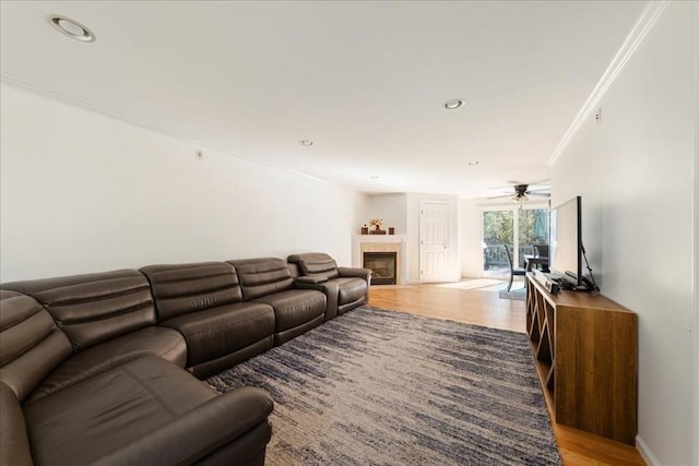 living area featuring a ceiling fan, a tiled fireplace, crown molding, light wood-style floors, and recessed lighting