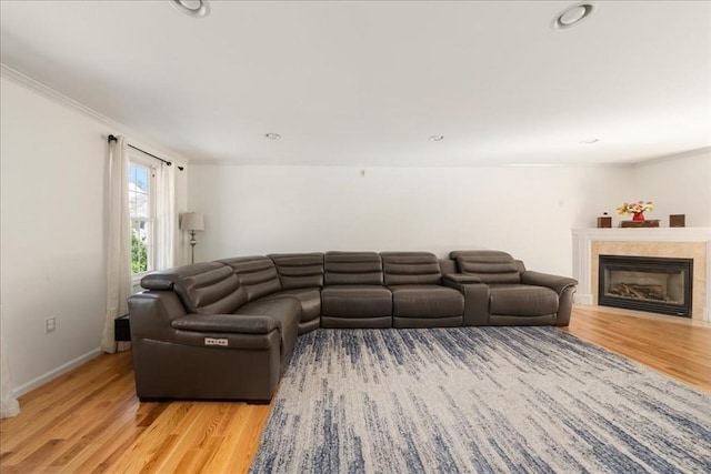 living room featuring light wood-style floors, baseboards, ornamental molding, and a fireplace with flush hearth