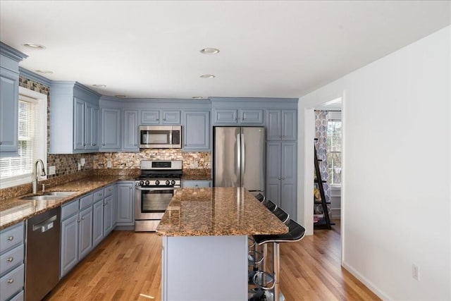kitchen with a kitchen bar, appliances with stainless steel finishes, a center island, a sink, and dark stone countertops