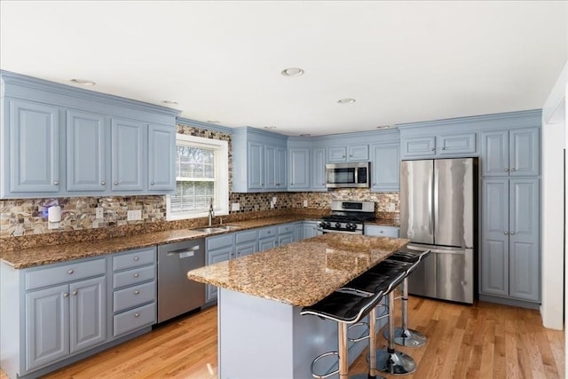 kitchen with dark stone counters, blue cabinets, a sink, light wood finished floors, and stainless steel appliances