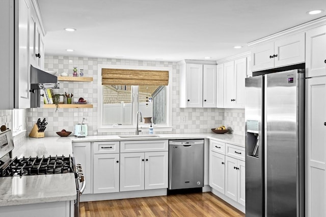 kitchen featuring appliances with stainless steel finishes, tasteful backsplash, white cabinetry, a sink, and extractor fan