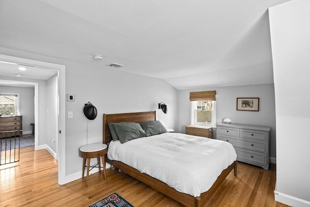 bedroom with baseboards, visible vents, light wood-style flooring, and lofted ceiling
