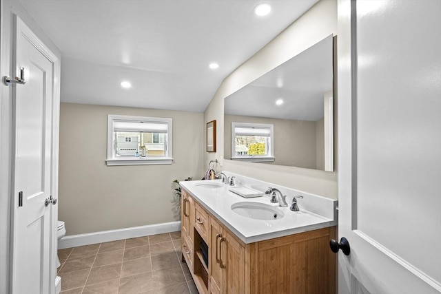 bathroom with baseboards, a sink, double vanity, and toilet