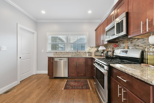 kitchen with sink, wood-type flooring, ornamental molding, appliances with stainless steel finishes, and light stone countertops