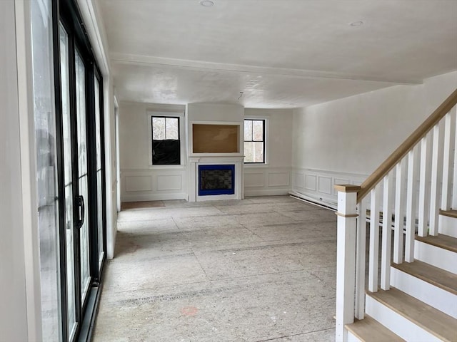 unfurnished living room with a wainscoted wall, a fireplace, stairway, and a decorative wall