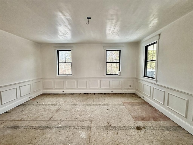 unfurnished room featuring a wainscoted wall and plenty of natural light