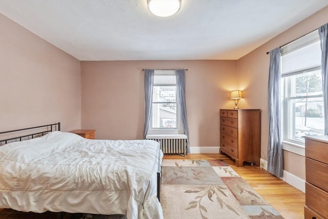 bedroom with multiple windows, radiator, and light wood-type flooring