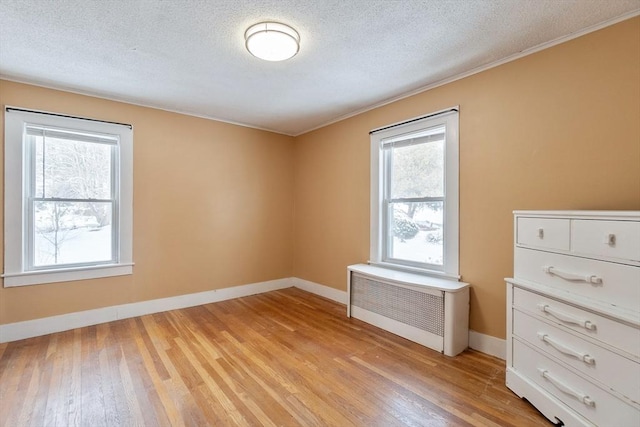 spare room featuring crown molding, radiator, a textured ceiling, and light wood-type flooring