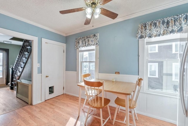 dining space featuring ceiling fan, light hardwood / wood-style flooring, ornamental molding, and a textured ceiling