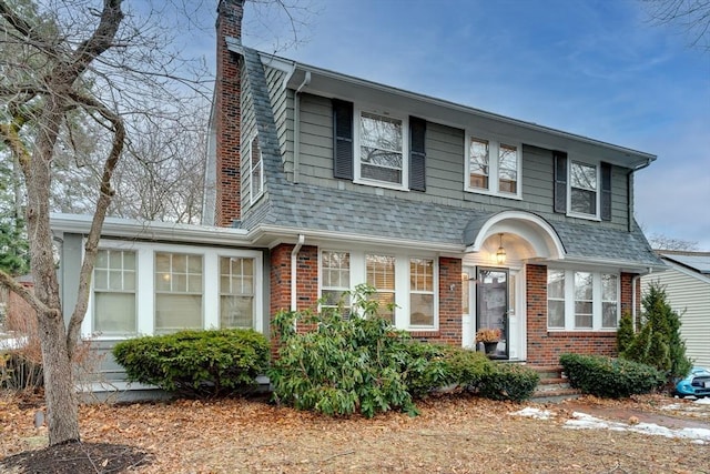 view of front of house featuring brick siding, a chimney, and roof with shingles