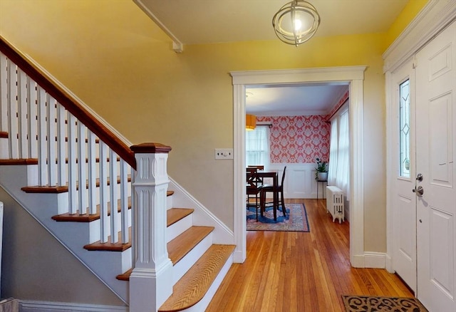 entryway with wallpapered walls, radiator heating unit, wood finished floors, baseboards, and stairs