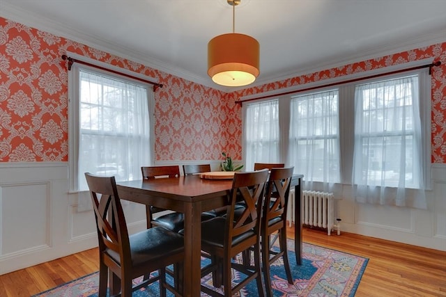 dining room featuring wallpapered walls, radiator heating unit, light wood finished floors, and a wainscoted wall