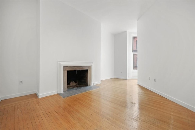 unfurnished living room with a fireplace with flush hearth, light wood-style floors, and baseboards