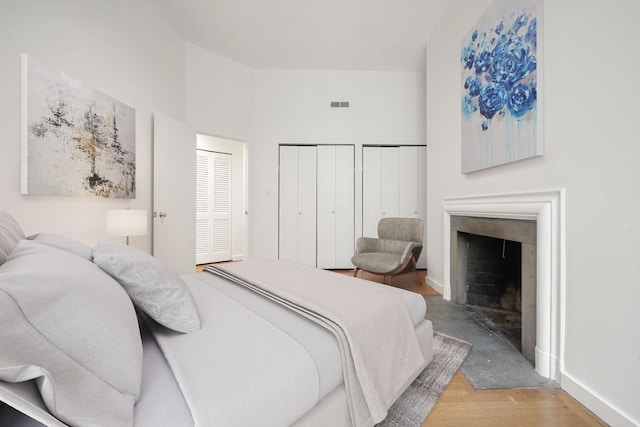 bedroom featuring visible vents, baseboards, two closets, wood finished floors, and a fireplace with flush hearth