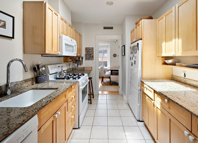 kitchen with light brown cabinetry, white appliances, stone countertops, and sink