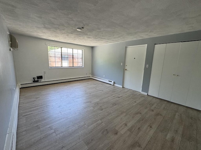 unfurnished bedroom featuring baseboard heating, a wall mounted air conditioner, a textured ceiling, multiple closets, and light wood-type flooring