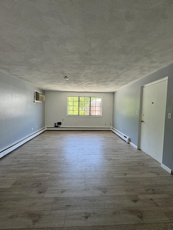 spare room with an AC wall unit, a baseboard heating unit, hardwood / wood-style floors, and a textured ceiling