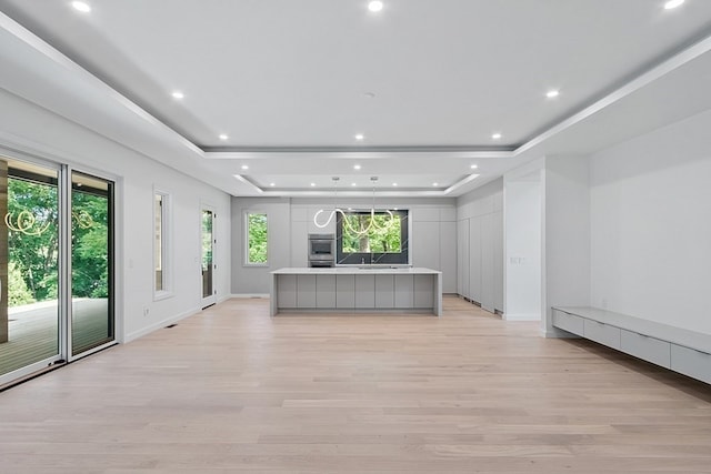 unfurnished living room featuring a raised ceiling, sink, and light hardwood / wood-style flooring