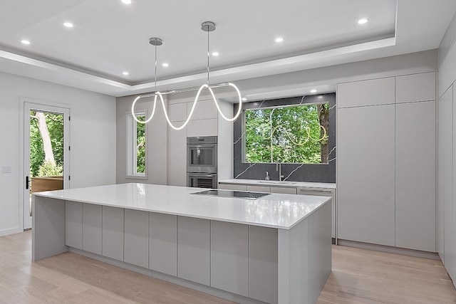 kitchen with a kitchen island, hanging light fixtures, a raised ceiling, and light wood-type flooring