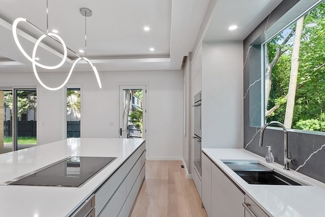 kitchen featuring light hardwood / wood-style floors, white cabinetry, black electric cooktop, sink, and a raised ceiling