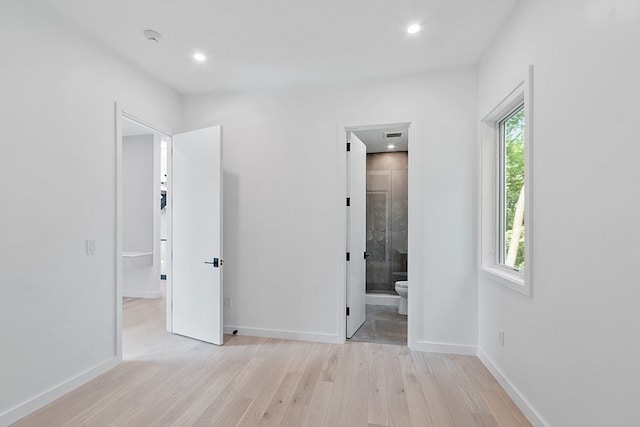 unfurnished bedroom with ensuite bath, multiple windows, and light hardwood / wood-style flooring