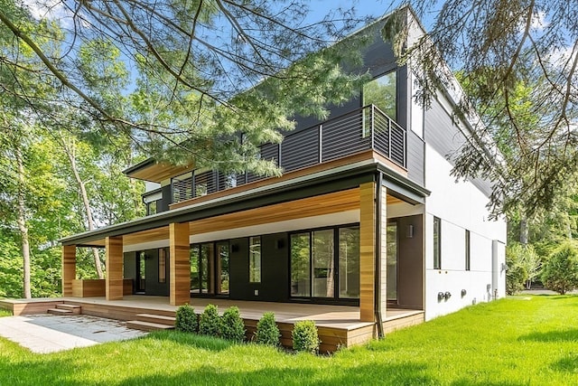 rear view of house with a lawn, a balcony, and a patio