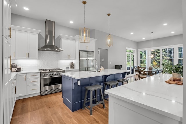 kitchen with white cabinets, premium appliances, a kitchen island with sink, wall chimney exhaust hood, and a kitchen bar