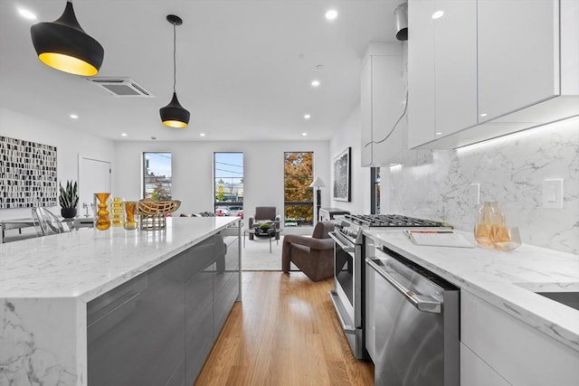 kitchen featuring hanging light fixtures, appliances with stainless steel finishes, open floor plan, white cabinets, and modern cabinets