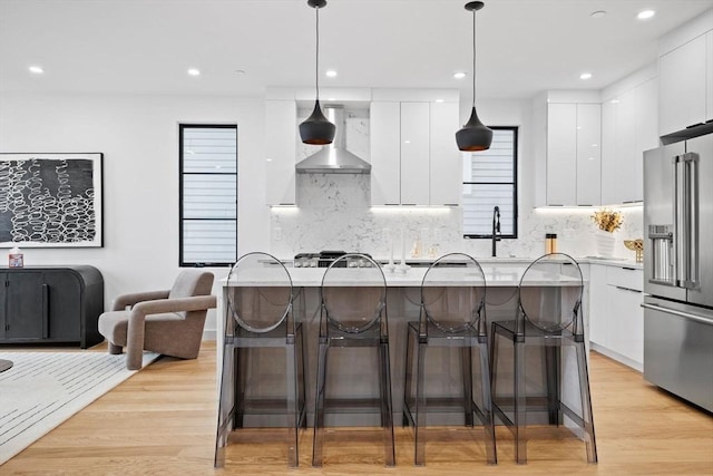 kitchen featuring wall chimney exhaust hood, high quality fridge, modern cabinets, light countertops, and pendant lighting