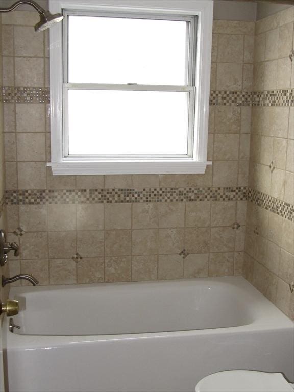 bathroom featuring toilet, tiled shower / bath combo, and a healthy amount of sunlight