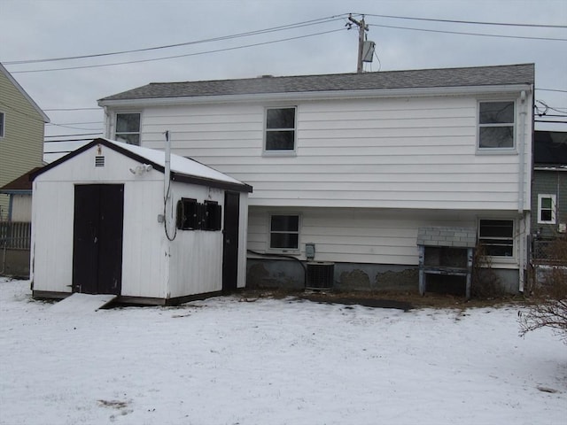 snow covered rear of property with cooling unit and a shed